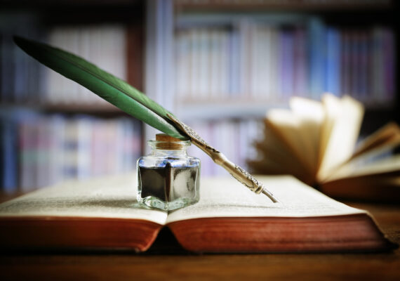 Quill pen and ink well resting on an old book in a library concept for literature, writing, author and history